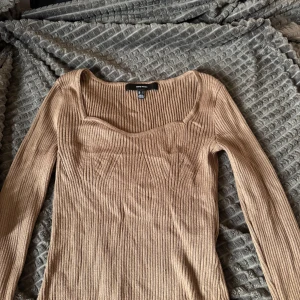 Ribbad beige långärmad tröja Vero Moda - Säljer en ribbad beige långärmad tröja från Vero Moda. Tröjan har en snygg fyrkantig ringning och figurnära passform som framhäver siluetten. Perfekt att styla med jeans eller kjol för en trendig look.