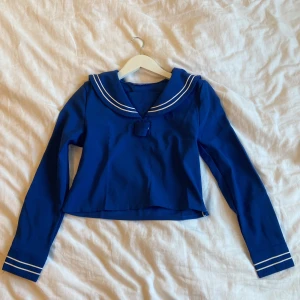 Marinblå sailor-blus med vita ränder - Säljer en marinblå sailor-inspirerad blus med långa ärmar och klassisk sjömanskrage (Ingår tillsammans med en vit scarf). Blusen har vita ränder på kragen och ärmsluten. Märket heter ”Fantasy Sheep” och köptes på Kawaii för 2 år sen. Perfekt för dig som gillar japansk stil!