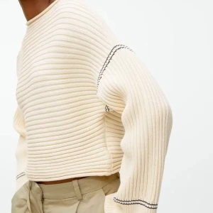 Ribbad beige tröja Arket - Ribbad stickad tröja från Arket i beige/creme med svarta kontrastsömmar. Tröjan har en loose passform, rund halsringning och långa ärmar. 