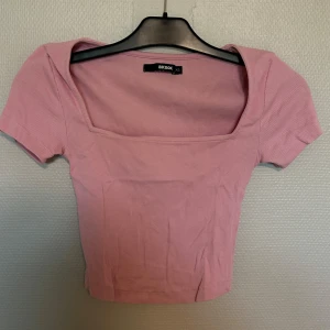 Rosa ribbad topp från Bik Bok - Supersöt rosa ribbad topp från Bik Bok med fyrkantig urringning och korta ärmar. Modellen är croppad och sitter tajt, perfekt till höga jeans eller kjol. Enkel men ändå trendig, passar dig som gillar en feminin och stilren look.