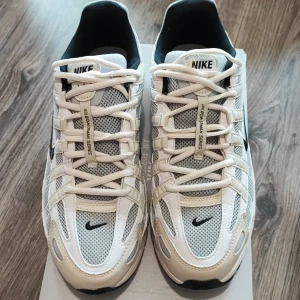 Nike P-6000 vita och grå sneakers - Nike P-6000 sneakers i vitt och grått med svarta detaljer. Ovandel i mesh och syntet med tydliga paneler och snörning. Swoosh-logga på sidan och P-6000-tryck vid hälen. Skön och sportig vibe, perfekt för dig som gillar retrostil.