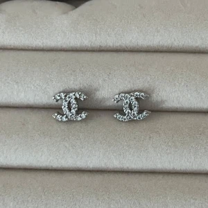 Örhängen - Snygga örhängeni klassisk CC-logga, täckta med glittrande strass. De är i silverfärg och ger en lyxig känsla till din look. Perfekta för dig som vill sticka ut med ikoniska accessoarer. 