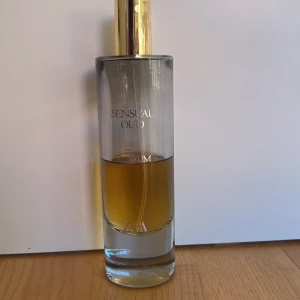 Zara Sensual Oud Eau de Parfum - En elegant parfymflaska från Zara med doften Sensual Oud. Flaskan är cylindrisk i glas med en guldig kork och transparent design som visar den gyllene vätskan inuti. Perfekt för dig som gillar lyxiga och varma dofter.