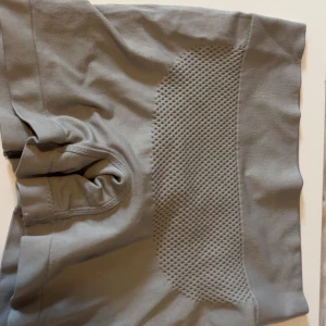 Grå seamless träningstights-shorts - Grå seamless shorts med hög midja och ribbade detaljer. Materialet är stretchigt syntet med meshpaneler för extra ventilation. Passformen är tight och designen är enkel men sportig, perfekt för gymmet eller annan träning.