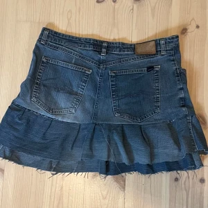 Jeanskjol med volang från MAC - Snygg blå jeanskjol från MAC med volang nertill och råa kanter. Midja: 40 cm