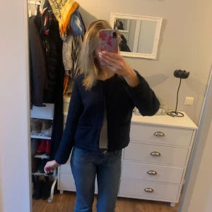 Mörkblå ”cardigan” jacka från Ellos - Säljer en mörkblå cardigan jacka från Ellos i storlek 40. Jackan är stickad med en mjuk struktur, har rund halsringning och är helfodrad på insidan. Enkel och stilren modell med lång ärm, perfekt att slänga på över en t-shirt eller topp.