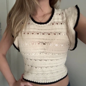 Beige virkad topp från H&M - Superfin beige virkad topp från H&M med svarta kanter. Toppen är ärmlös med volangliknande axlar och har ett genombrutet mönster som ger en luftig känsla. Perfekt till sommaren och enkel att styla med jeans eller kjol.