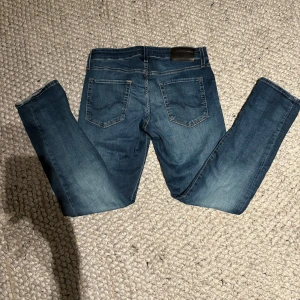 Slim/glenn jack&jones - Säljer ett par klassiska blå jeans från jack&jones i 30/30 med snygg tvätt och raka ben. Jeansen har fem fickor, kontrastsömmar och en mörk läderpatch bak i midjan. Perfekta för dig som gillar en enkel och stilren look.