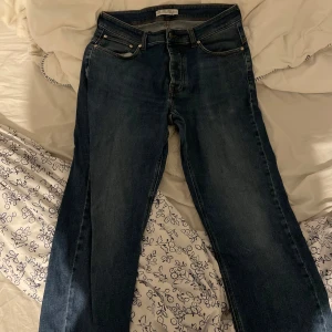 Mörkblå jeans från The Blue Uniform - Snygga mörkblå jeans från The Blue Uniform med klassisk femficksdesign och raka ben. Jeansen har kontrastsömmar och en stilren läderpatch bak i midjan. Perfekta för dig som gillar en enkel och tidlös look.