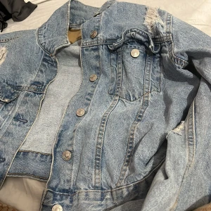 Ljusblå jeansjacka från 157 - Säljer en klassisk ljusblå jeansjacka från 157 med slitna detaljer och snygga silverfärgade knappar. Jackan har bröstfickor med lock och en cool vintagekänsla. Perfekt för dig som gillar streetstyle och vill ha en tidlös look.