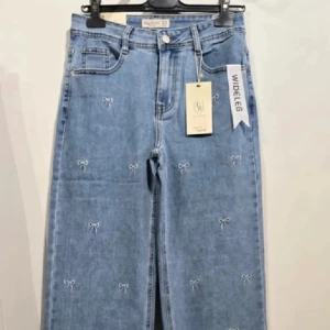 Blå wide leg jeans med broderade rosetter - Snygga ljusblå wide leg jeans från FR med broderade små vita rosetter över hela byxorna. Klassisk femficksmodell med hög midja och raka, vida ben. Perfekta för dig som vill ha en söt och trendig twist på dina jeans.