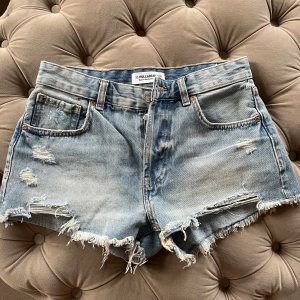 Blå jeansshorts från Pull&Bear - Snygga blå jeansshorts från Pull&Bear med slitna detaljer och fransiga kanter. Perfekta för en avslappnad stil. De har en klassisk femficksdesign och knappgylf.