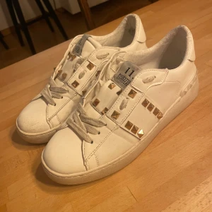 Valentino skor  - Snygga vita sneakers från Valentino med guldiga nitar. Skorna har snörning och är perfekta för en stilren look. Passar bra till både jeans och klänning. Köpte de på vinted så har därav inget kvitto 