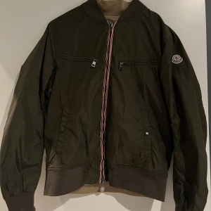 Olivgrön moncler jacka  - Säljer denna snygga moncler jacka då den ej kommer till någon användning längre samt börjar bli för liten, jackan är i väldigt fint skick. Någon fundering eller liknande så är det bara att skriva. Sitter ca strl 170-178. Pris kan diskuteras 