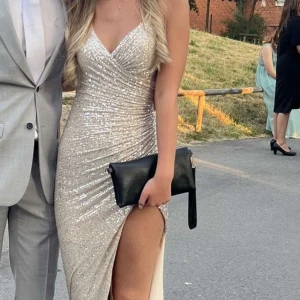 Glittrig balklänning  - Säljer en fantastisk glittrig långklänning i champagnefärg med en djärv slits och öppen rygg. Klänningen har smala axelband och en figurnära passform som framhäver silhuetten. Perfekt för bal osv. Nypris:2500kr