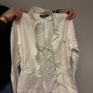 Vit skjorta från Polo Ralph Lauren - Klassisk vit skjorta från Polo Ralph Lauren med broderad logga på bröstet. Skjortan har långa ärmar och knappar framtill. Perfekt för en stilren look.
