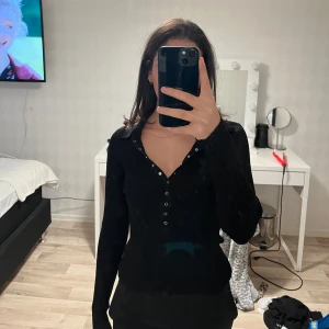 Svart ribbad tröja från Zara - Snygg svart ribbad tröja från Zara med knappar framtill och en klassisk krage. Perfekt för en stilren look. Tröjan har långa ärmar och en figurnära passform.