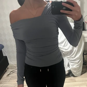 Grå offshoulder topp - Snygg grå offshoulder topp med långa ärmar. Perfekt för en stilren look. Materialet är mjukt och bekvämt. Tröjan är helt ny men etiketten sitter inte kvar.