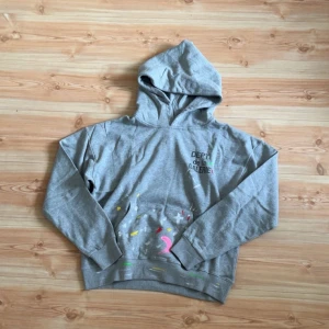 Gallery dept - Säljer en grå hoodie med färgglada detaljer och text. Tröjan har en klassisk huva och långa ärmar, perfekt för en avslappnad stil.