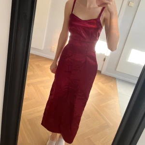 Vinröd sidenklänning - Elegant vinröd klänning i siden med smala axelband och figurnära passform. Slits vid benet. Perfekt för festliga tillfällen.