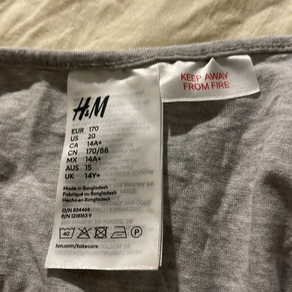 Säljer en grå linnetopp från H&M med texten 'New York USA' tryckt på framsidan. Toppen har smala axelband och en enkel design som passar perfekt för en avslappnad stil.. Yläosat.