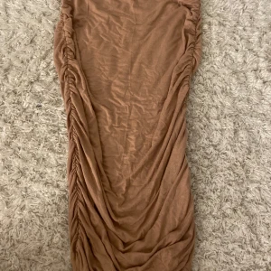 Beige kjol från Boohoo - Säljer en snygg beige kjol från Boohoo med rynkade detaljer längs sidorna. Kjolen har en smickrande passform och är perfekt för olika tillfällen. Storlek EU 36.