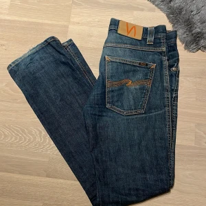 Mörkblå Nudie jeans - Mörk blå Nudie jeans i mycket bra skick med slitningar vid benöppningens baksida (bild 4&5). Faller RIKTIGT SNYGGT på skor, men säljer eftersom jag tycker de är för liten midja storlek för mig. Modell: Low Slim Jim