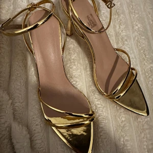 Guldiga klackskor med remmar - Helt nya guldiga klackskor med smala remmar och spetsig tå. Perfekta för en festlig kväll. Justerbara spännen runt ankeln för bästa passform. Aldrig använda då jag beställde fel storlek och tiden för returnera gick ut.