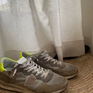 Grå sneakers från Philippe Model - Snygga grå sneakers från Philippe Model med kamouflagemönster och neongula detaljer. Skorna har snörning och en bekväm passform. Perfekta för en stilren och avslappnad look.