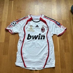 Vit AC Milan fotbollströja med Kaka 22 - Säljer en vit retro AC Milan fotbollströja från Adidas med Kaka's namn och nummer 22 på ryggen. Tröjan har röda och vita detaljer samt Champions League-märke. Perfekt för fans av Kaka och AC Milan! Rikitg dessutom