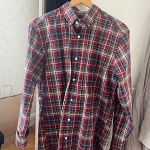 Rutig skjorta från Gant - Säljer en snygg rutig skjorta från Gant i rött, blått och vitt. Skjortan har långa ärmar och knappar framtill. Perfekt för en stilren look.