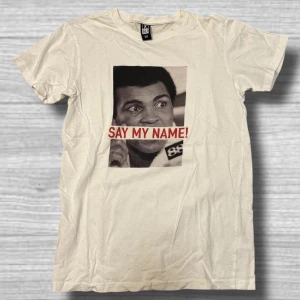 Vit t-shirt med tryck - Säljer en vit t-shirt från All med ett coolt tryck av en känd person och texten 'Say My Name!' i rött. Perfekt för dig som vill ha en statement piece i garderoben. 👕