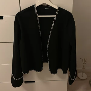Svart jacka från Gina Tricot - Snygg svart jacka/kofta från Gina Tricot med vita sömmar längs kanterna. Aldrig använd, dock ingen prislapp kvar. Pris kan diskuteras, kom privat för fler bilder☺️