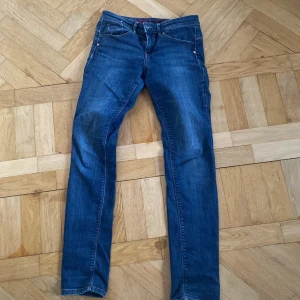 Blå jeans med knappdetalj - Snygga blå jeans med en unik knappdetalj i metall. Relativt nya och nästan oanvända, inga fläckar. Frågor? Kontakta mig på Plick!