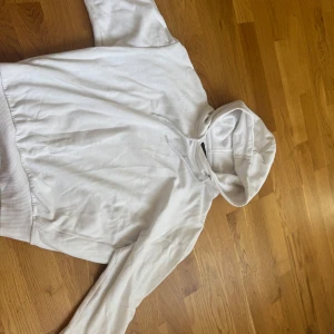 Vit hoodie - Säljer en klassisk vit hoodie med långa ärmar och en bekväm huva. Perfekt för en avslappnad stil. Den har ribbade muddar vid ärmslut och nederkant.