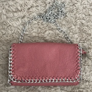 Rosa axelväska från Tiamo - Snygg rosa axelväska från Tiamo med silverkedja och dekorativa sömmar runt kanterna. Perfekt för att ge en färgklick till din outfit. Endast använd ett fåtal gånger 💞