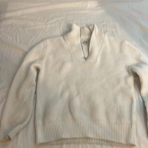 Vit stickad tröja  - Säljer en stilren vit stickad tröja från H&M med en hög krage och dragkedja. Tröjan har långa ärmar och en ribbad struktur som ger en klassisk look. Perfekt för kyligare dagar.