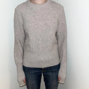 Beige stickad tröja från COS - Säljer en stilren beige stickad tröja från COS i 100% ull. Tröjan har en klassisk rund halsringning och långa ärmar med ribbade muddar. Perfekt för kyligare dagar.