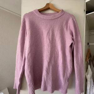 Ljusrosa stickad tröja - Mysig ljusrosa stickad tröja med ribbade detaljer vid hals, ärmslut och nederkant. Perfekt för kyliga dagar och ger en mjuk och bekväm känsla. Passar bra till både jeans och kjol.