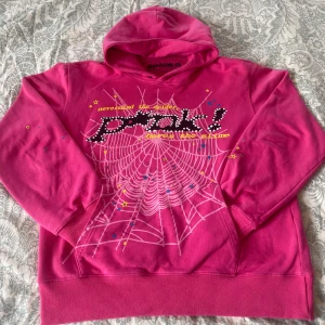 Rosa SP5DER Hoodie🕷️🕸️ - Säljer en cool rosa hoodie från SP5DER med ett spindelnätsmönster och textdetaljer på framsidan. Hoodien har långa ärmar och en bekväm passform.