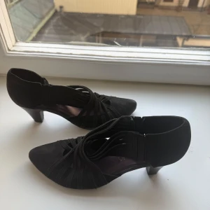 Svarta klackar - Snygga svarta klackae med spetsig tå. Skorna har en unik design med snörning som ger en stilren look. Perfekta för en kväll ute eller en speciell tillställning. Har en resåreffekt på sidan (se bild). Har använts några gånger 