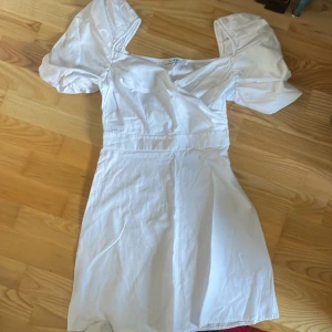Vit klänning med puffärmar - Säljer en stilren vit klänning med puffiga kortärmar och en v-ringad design. Perfekt för sommarens alla tillfällen. Klänningen har en smickrande passform och är gjord i ett lätt material.