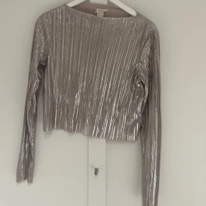   topp med metalliska skiftningar från H&M - Snygg silverfärgad topp från H&M med glittrig finish. Toppen har långa ärmar och en croppad passform, perfekt för en festlig look. Materialet är syntetiskt och ger en lyxig känsla. Ett måste för garderoben!