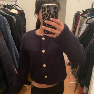 Mörkblå kofta med guldknappar - Säljer en mörkblå kofta från Bik Bok med eleganta guldknappar framtill. Koftan har en mjuk och fluffig textur, perfekt för kyligare dagar. Den är croppad och har långa ärmar, vilket ger en stilren look. Passar bra till både jeans och kjol.