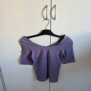 Lila offshoulder topp - Säljer en snygg lila offshoulder topp med korta ärmar. Perfekt för en somrig look eller en kväll ute. Toppen har en enkel och stilren design som passar till många olika outfits.