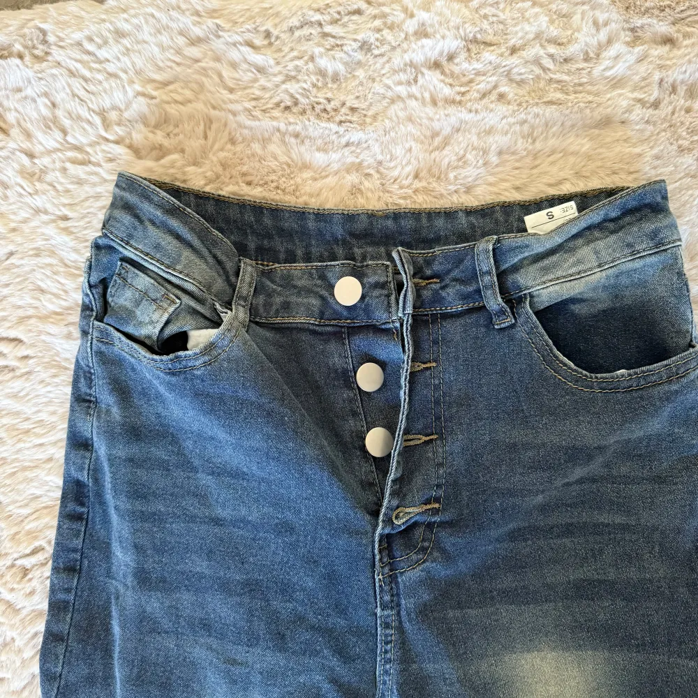 Snygga blå bootcut jeans med hög midja och knappar framtill. Perfekta för en avslappnad stil med en touch av retro. De har en klassisk femficksdesign och en lätt tvättad look.. Farkut & Housut.