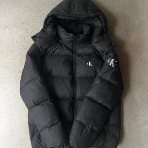 Ck puffer jacka  - Snygg svart pufferjacka från Calvin Klein. Den är köpt för 2699kr men använd i 1-2 månader nu. Finns lite lite små fläckar (sista bilden). Perfekt för kyliga dagar med sin vadderade design.