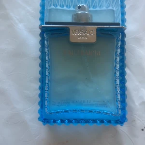 Versace Man Eau Fraîche Parfym - Säljer en elegant Versace Man Eau Fraîche parfym i en stilren blå glasflaska med silverdetaljer. Flaskan rymmer 100 ml och har en modern design med räfflade kanter. Perfekt för den som söker en fräsch och sofistikerad doft. Men den har 50ml kvar