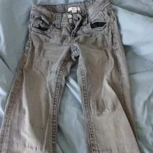 Grå jeansbyxor - Säljer ett par grå jeansbyxor med klassisk femficksdesign och knappgylf. Byxorna har en rak passform och är perfekta för en avslappnad stil. De är tillverkade i ett slitstarkt material som ger en bekväm känsla hela dagen.