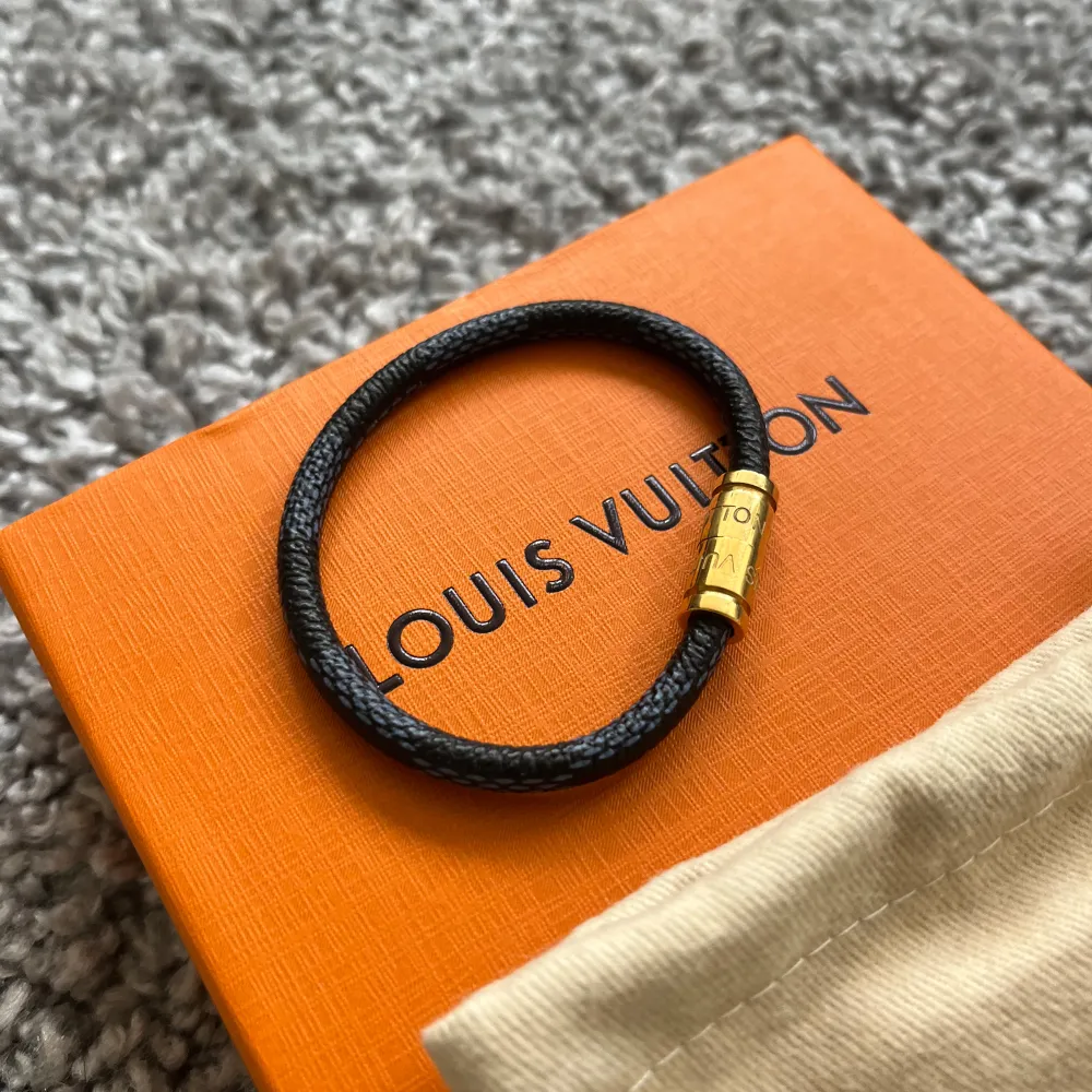 Elegant svart armband från LV med en stilren design. Armbandet har en guldig låsdetalj som ger en lyxig touch. Perfekt accessoar för att komplettera din look.. Asusteet.